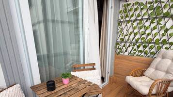 Un balcon avec une table en bois, une chaise en osier, un pot de fleurs et un coussin blanc.