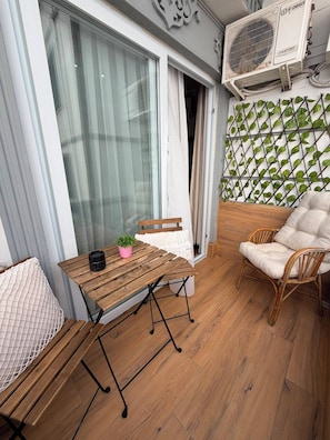 Un balcon avec une table en bois, une chaise en osier, un pot de fleurs et un coussin blanc.