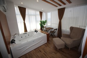 A modern bathroom with a large bathtub, wooden flooring, and a seating area with a table and chairs.