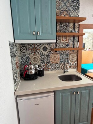 A kitchen with teal cabinets, patterned backsplash, and a white refrigerator.