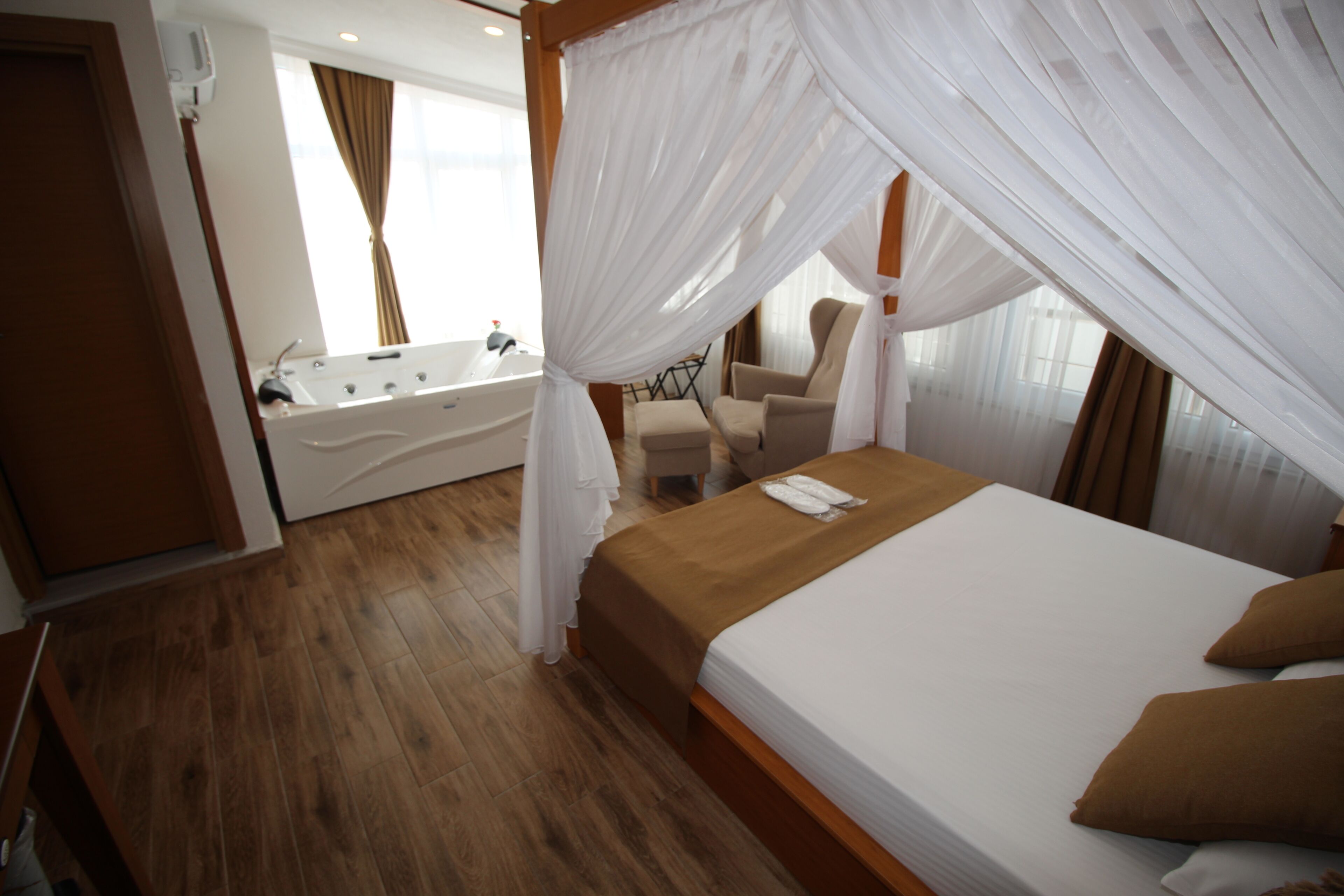 Une chambre à coucher avec un lit à baldaquin, un coin salon avec un fauteuil et une table, et une salle de bain séparée avec une baignoire.