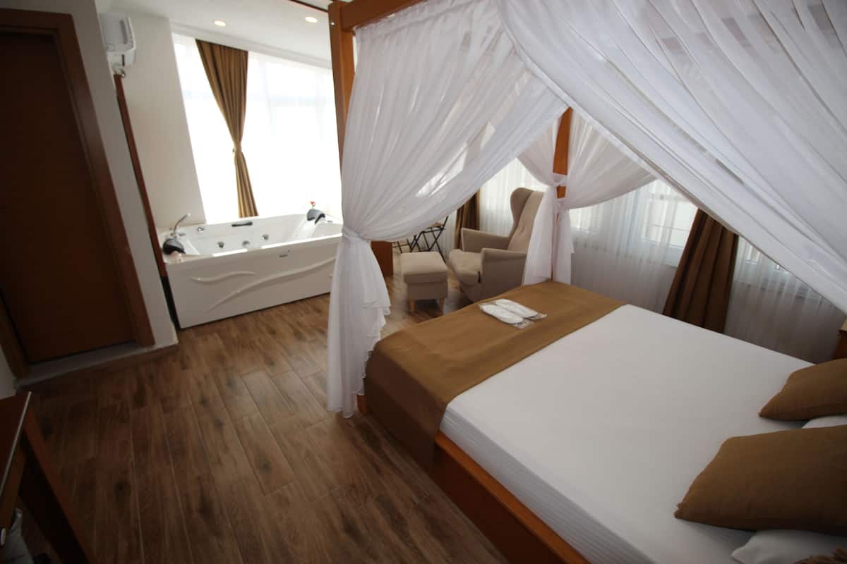 Ein Schlafzimmer mit Baldachinbett, einer Sitzecke mit Stuhl und Tisch sowie einem eigenen Badezimmer mit Badewanne.