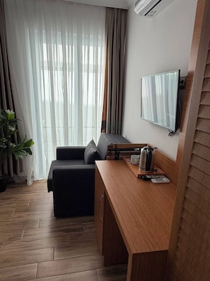 Une chambre moderne équipée d’un canapé, d’un bureau en bois, d’une machine à café, d’une télécommande et d’un téléviseur fixé au mur.