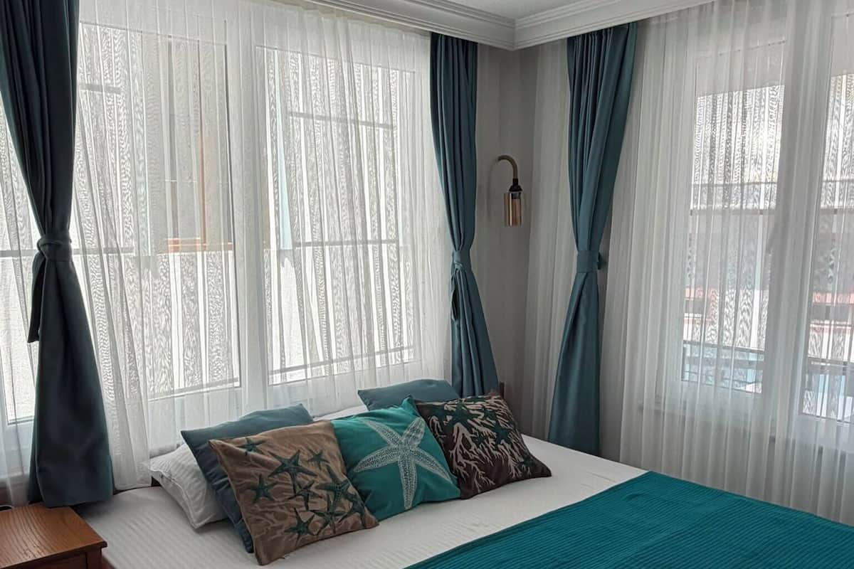 Ein Schlafzimmer mit Bett, Vorhängen, einem Nachttisch und einer Wandlampe.