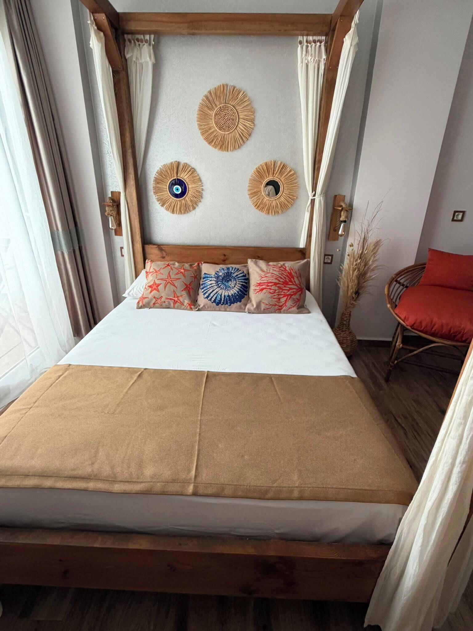 Un lit avec une tête de lit en bois, trois éléments décoratifs fixés au mur et une chaise rouge.