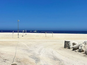 Una playa arenosa con cielo azul despejado, algunas embarcaciones y una estructura de piedra.