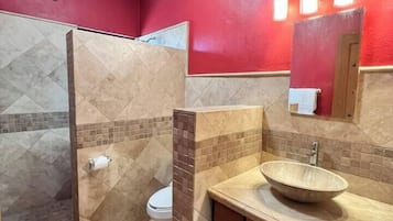 Un baño con lavamanos color beige, un espejo y una ducha con azulejos color beige.