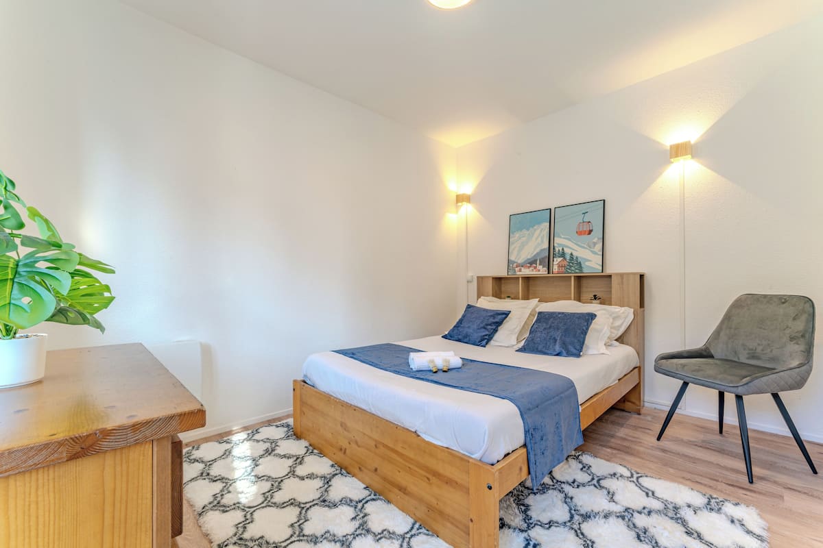 Un dormitorio con una cama de madera, dos lámparas de pared, una silla y una planta.