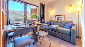 Una habitación acogedora con una mesa de comedor, sillas, un sofá y vistas a montañas a través de amplias ventanas.
