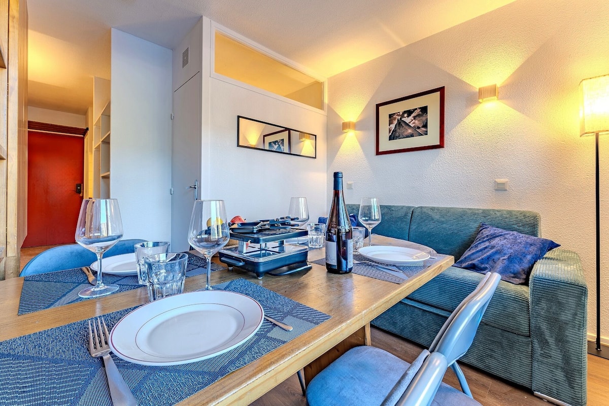 Un comedor con una mesa preparada para dos, una botella de vino y un sofá al fondo.