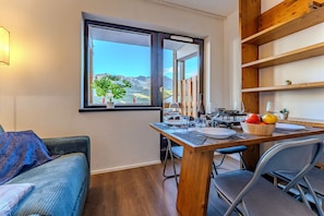 A dining area with a table set for two, a view of mountains through a window, and a wooden shelf with a plant.