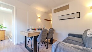 Una sala de estar moderna con un sofá gris, una mesa de comedor con sillas y una pequeña cocina.
