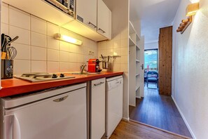 A narrow kitchen with white cabinets, a red countertop, and a view into a dining area with a table and chairs.