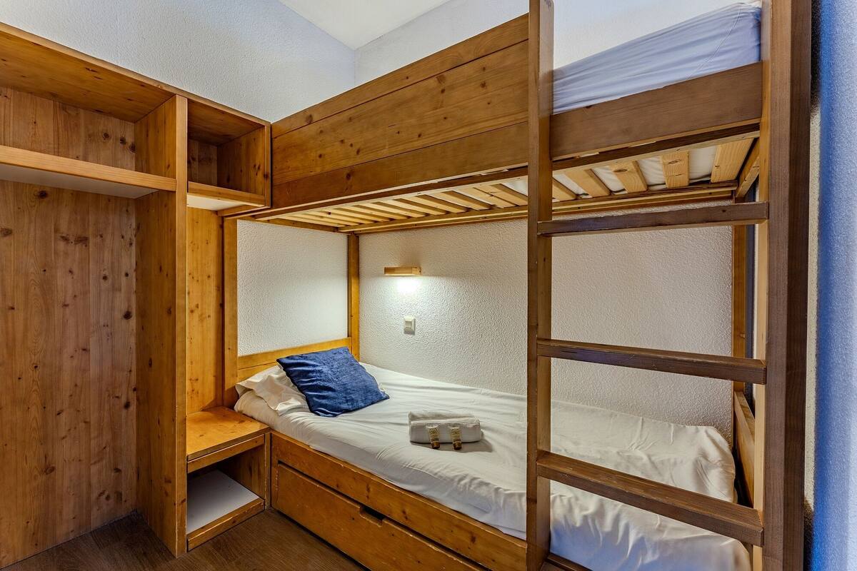 Habitación con literas, cabecero de madera, mesita de noche y lámpara de pared.