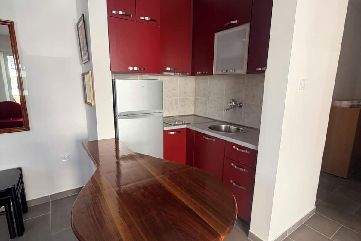A modern kitchen with red cabinets, a white countertop, and a built-in microwave.