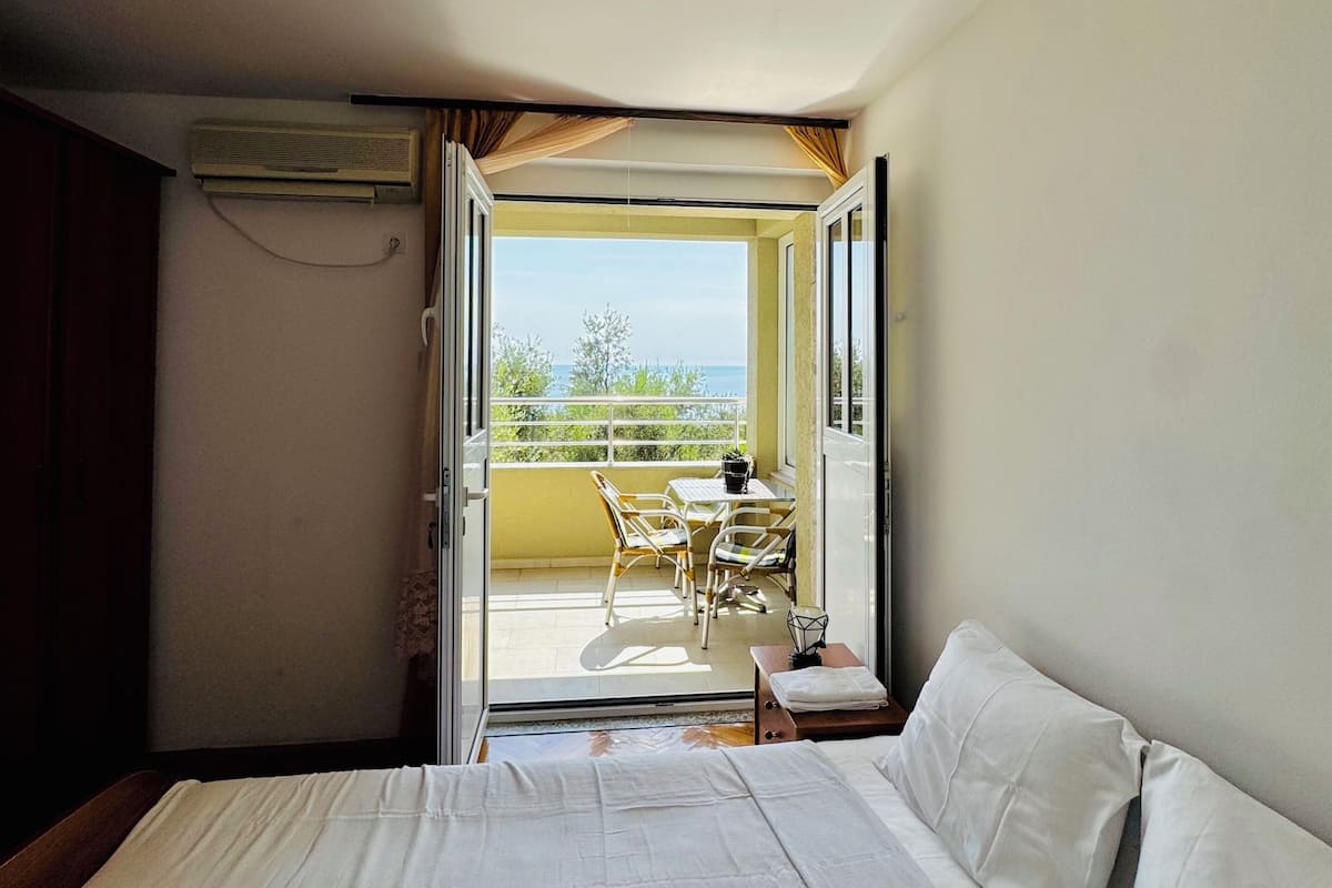 A hotel room with a bed, a small table with chairs, and a balcony with a view.