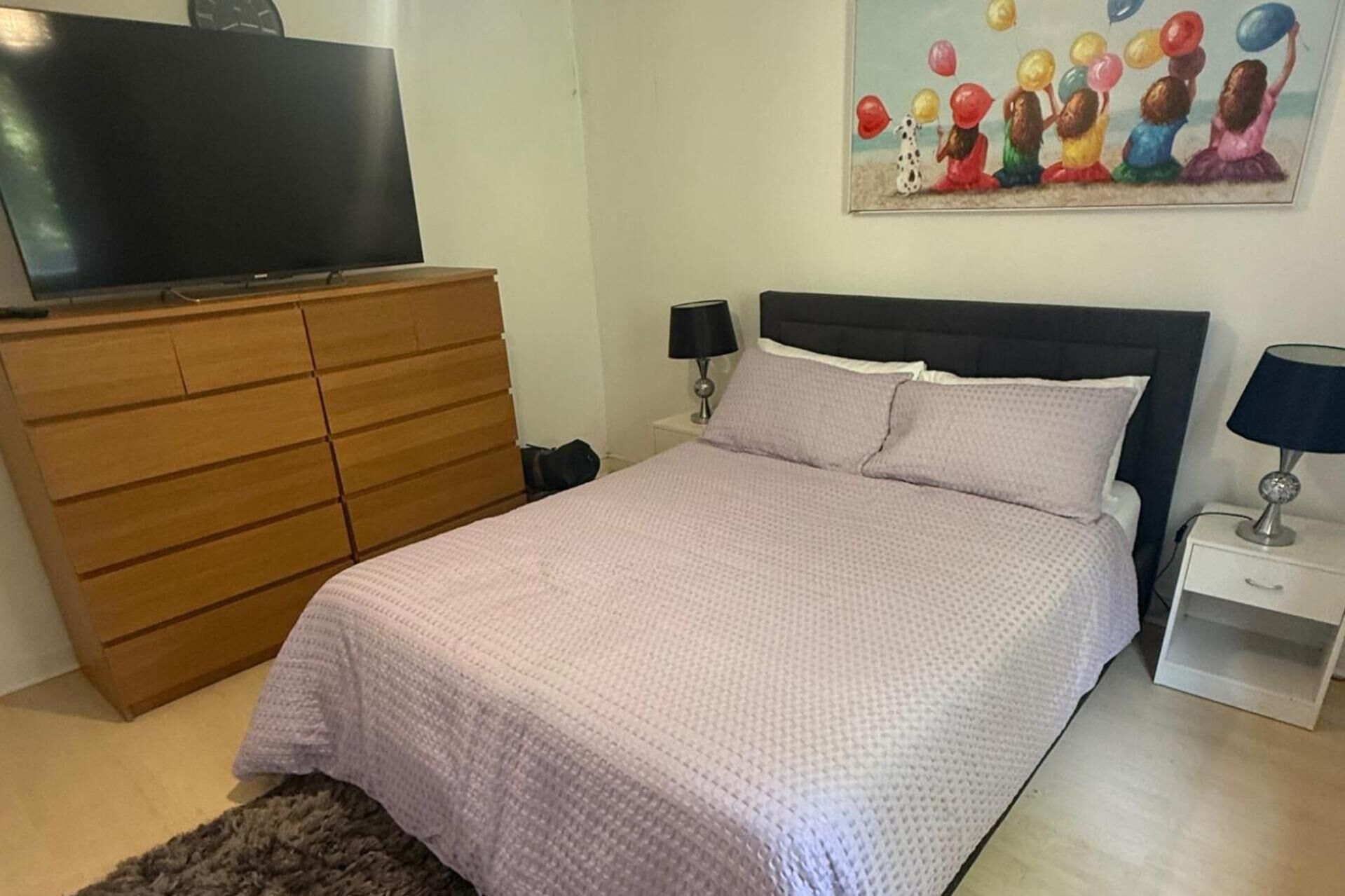 A bedroom with a bed, a dresser, a nightstand, a lamp, and a painting on the wall.