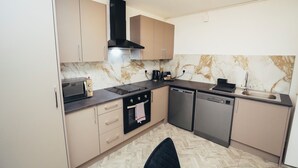 Una cucina moderna con mobili color beige, una cappa aspirante nera, un forno a microonde, un forno, una lavastoviglie e uno schienale in marmo.