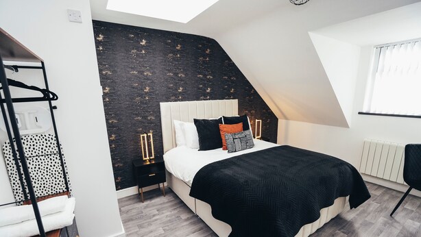 Una camera da letto moderna con soffitto spiovente, un letto con copripiumino bianco e nero, un muro con motivo scuro e un termosifone bianco.