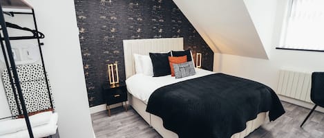 Un dormitorio moderno con techo inclinado, una cama con colcha blanco y negro, pared con diseño oscuro y radiador blanco.