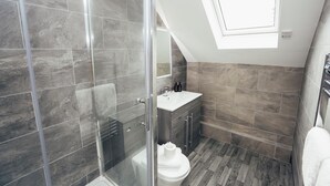 Un bagno moderno con cabina doccia in vetro, un water bianco, un mobile lavabo con specchio e un lucernario.