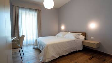 A bedroom with a bed, bedside table, chair, and a large window with curtains.