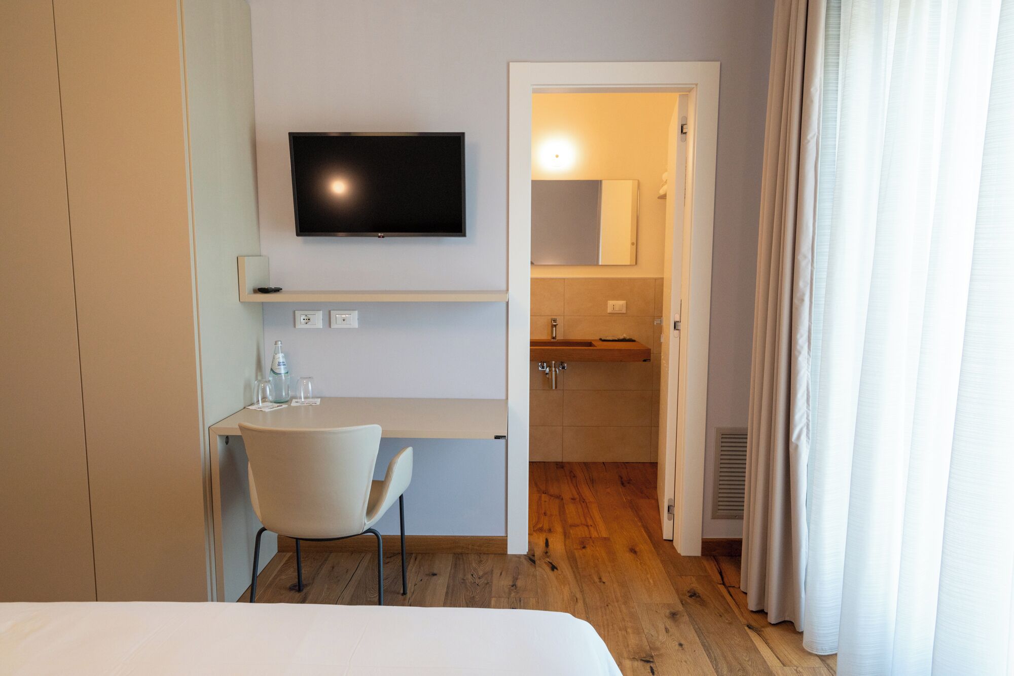 Habitación de hotel con cama, escritorio con silla, televisión y baño visible a través de una puerta abierta.