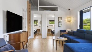 A modern interior with a TV, wooden furniture, a sofa, a table, and a view of a garden through large windows. - VillaVilla 980 - Juelsminde, Østjylland (Juelsminde)