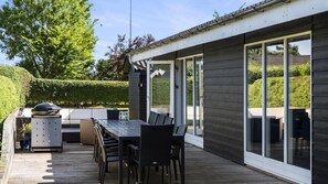 Eine moderne Außenpatio mit Esstisch und Stühlen, einem Grill und einer großen Glasschiebetür.