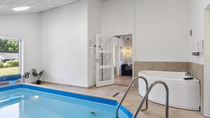 A modern indoor pool area with a clear view of the pool, a separate bathroom with a bathtub, and a door leading to another room. - VillaVilla 980 - Juelsminde, Østjylland (Juelsminde)