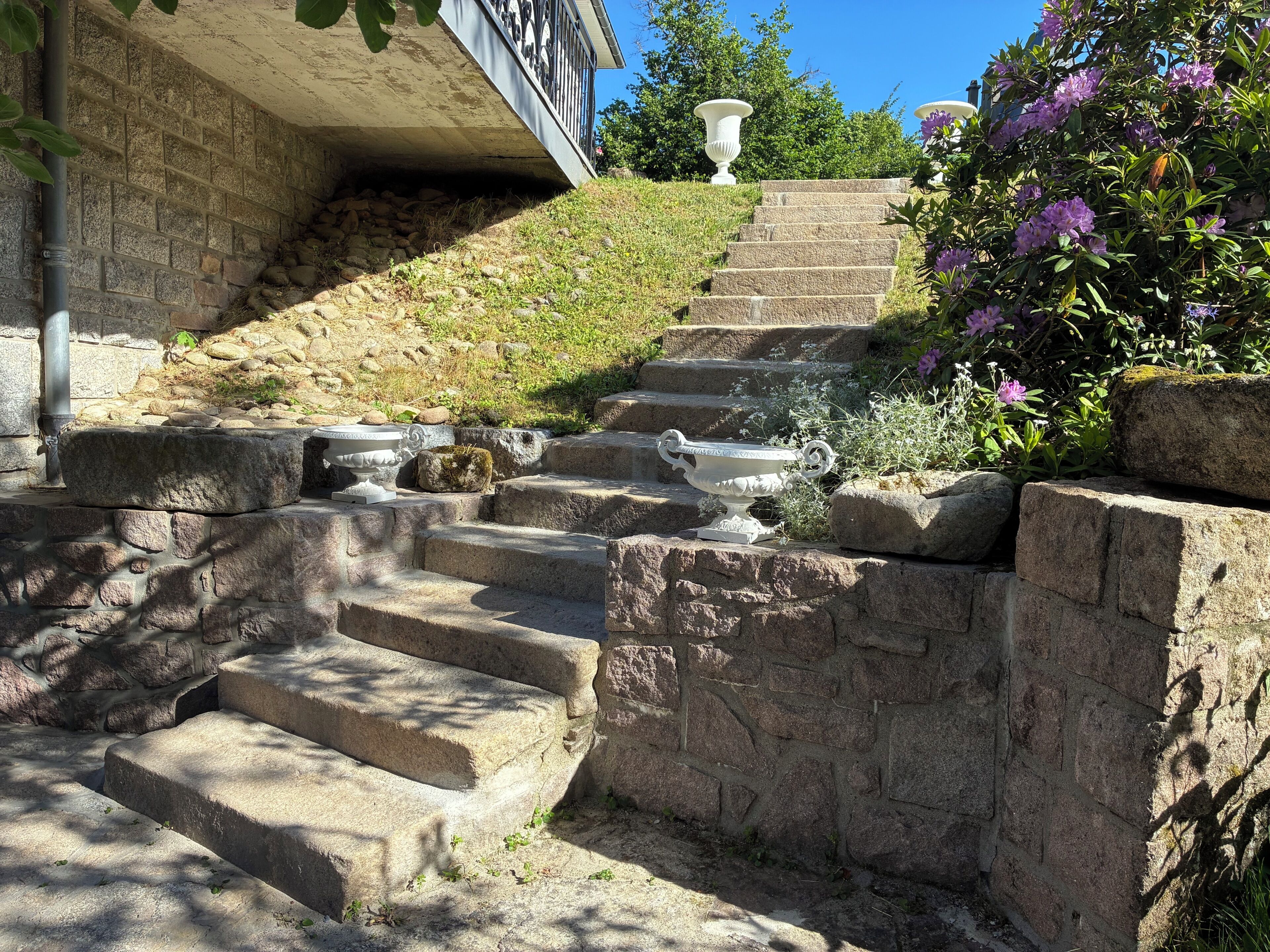 A stone staircase with steps leading up to a building, surrounded by greenery and decorative urns.