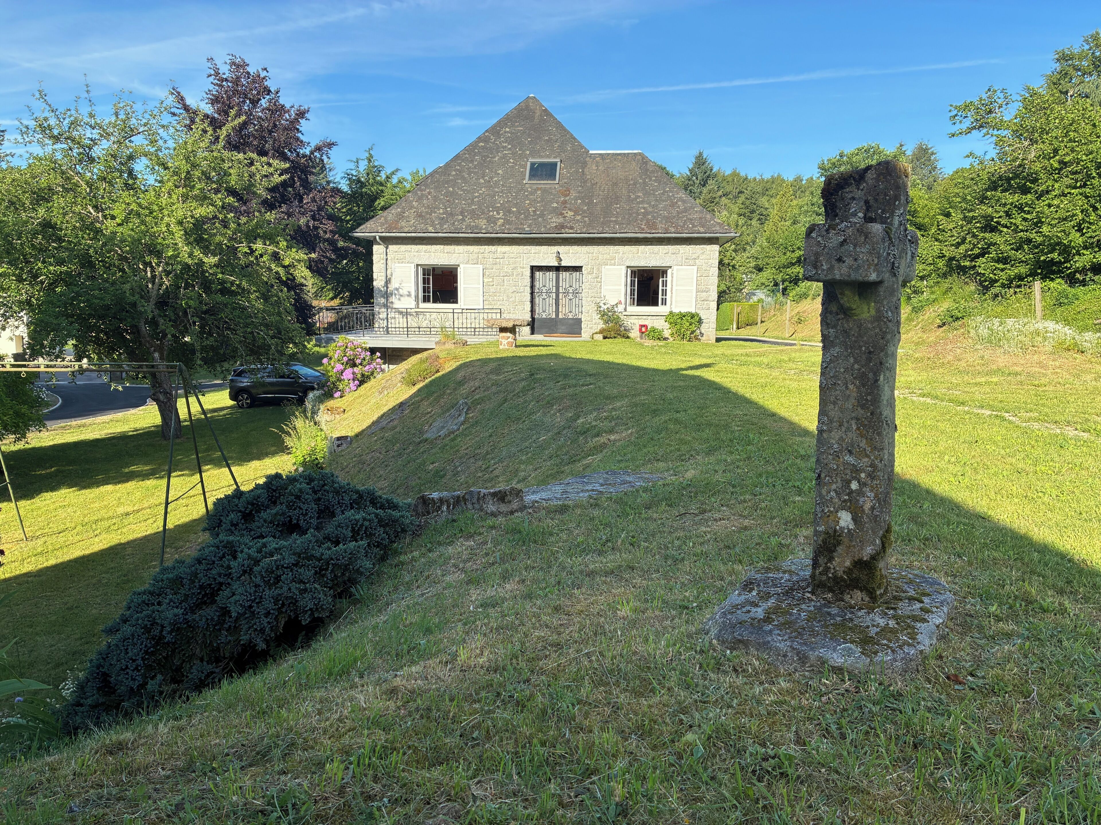 Una casa de piedra con techo inclinado, un camino de entrada y un patio cubierto de césped con una construcción de piedra.