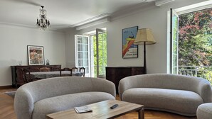 A living room with a wooden coffee table, two grey sofas, a chandelier, a dining table with chairs, and a large window with a view of trees. - House for 8 people in Meymac with electric bikes (Meymac)