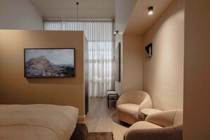 Ein modernes Hotelzimmer mit einem Bett, zwei Sesseln, einem Gemälde und einem großen Fenster mit Vorhängen.