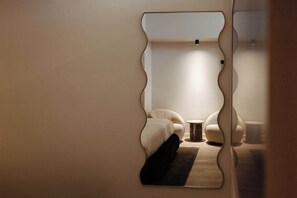 Ein Zimmer mit einem außergewöhnlichen, wellenförmigen Spiegel, einem kleinen runden Tisch und zwei bequemen Sesseln.