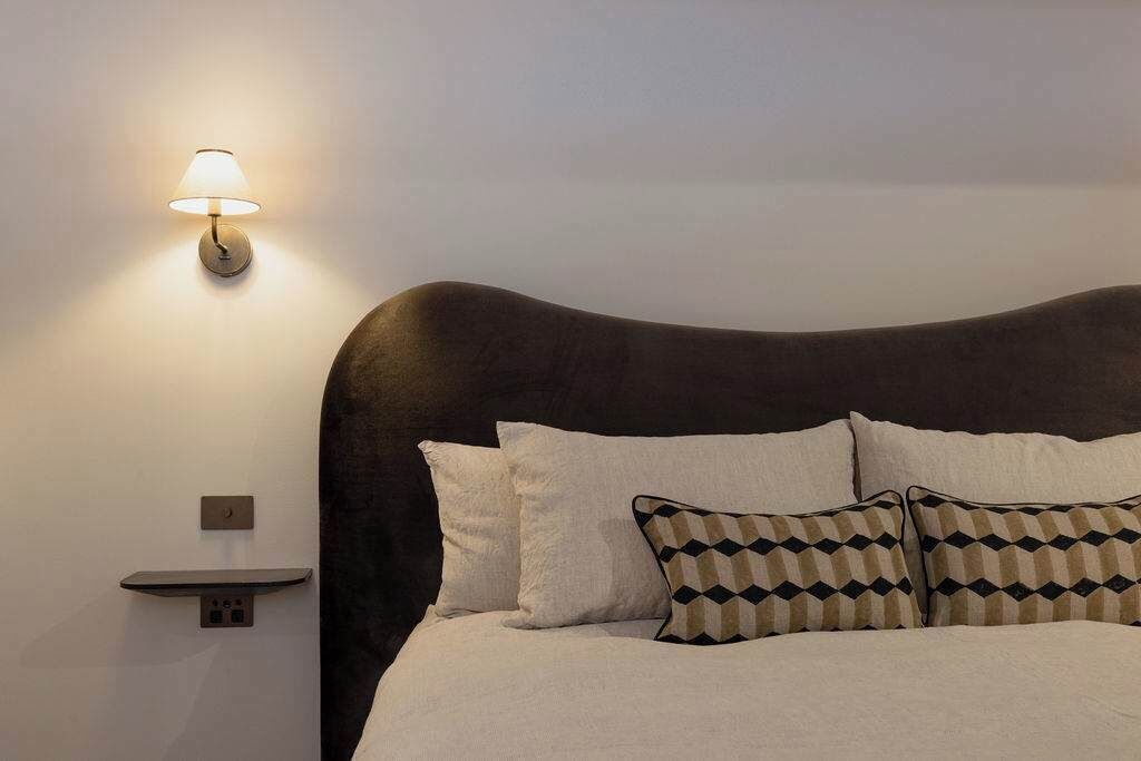 Een bed met een donker hoofdeinde, wit beddengoed en gestreepte kussens.