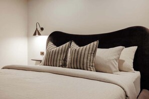 Ein Bett mit dunkelbrauner Kopfteil, zwei gestreifte Kissen und ein schlichtes weißes Kissen.