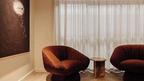 Ein Zimmer mit zwei Samt-Sesseln, einem kleinen Holztisch und einem großen, abstrakten Gemälde an der Wand.
