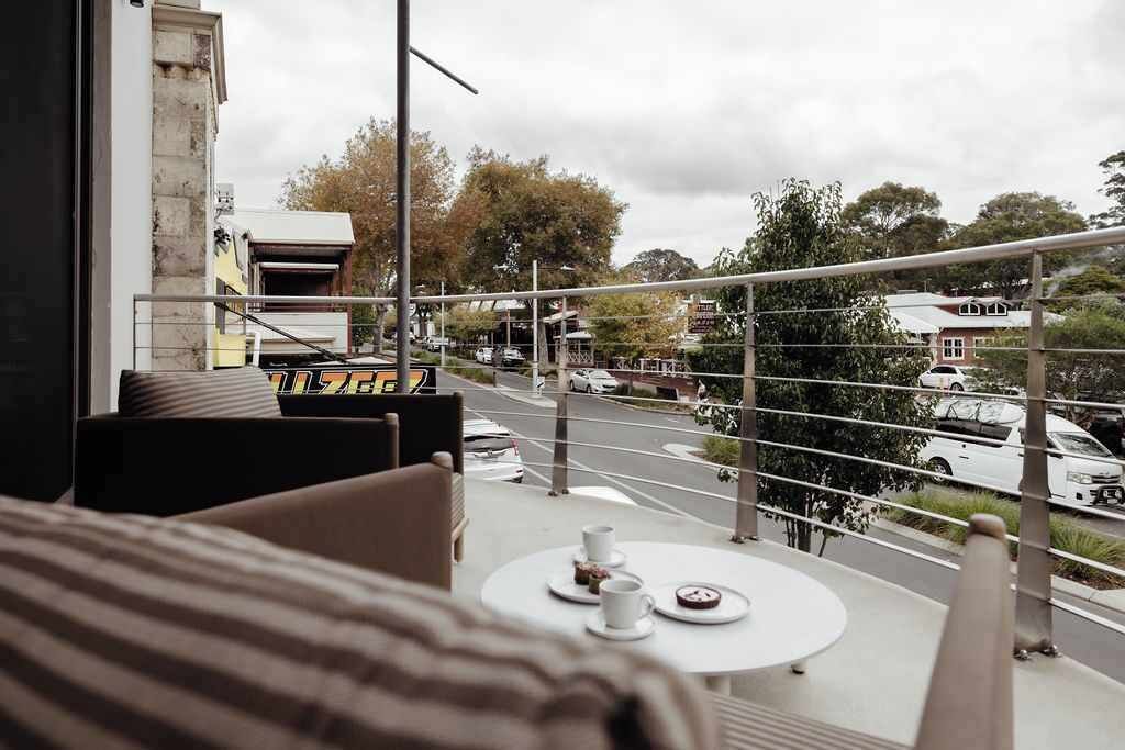 A balcony with a table and chairs, overlooking a street with parked cars and buildings.