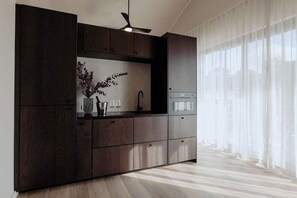 Eine moderne Küche mit dunklen Schränken, einem eingebauten Backofen und einem Fenster mit transparenten Vorhängen.