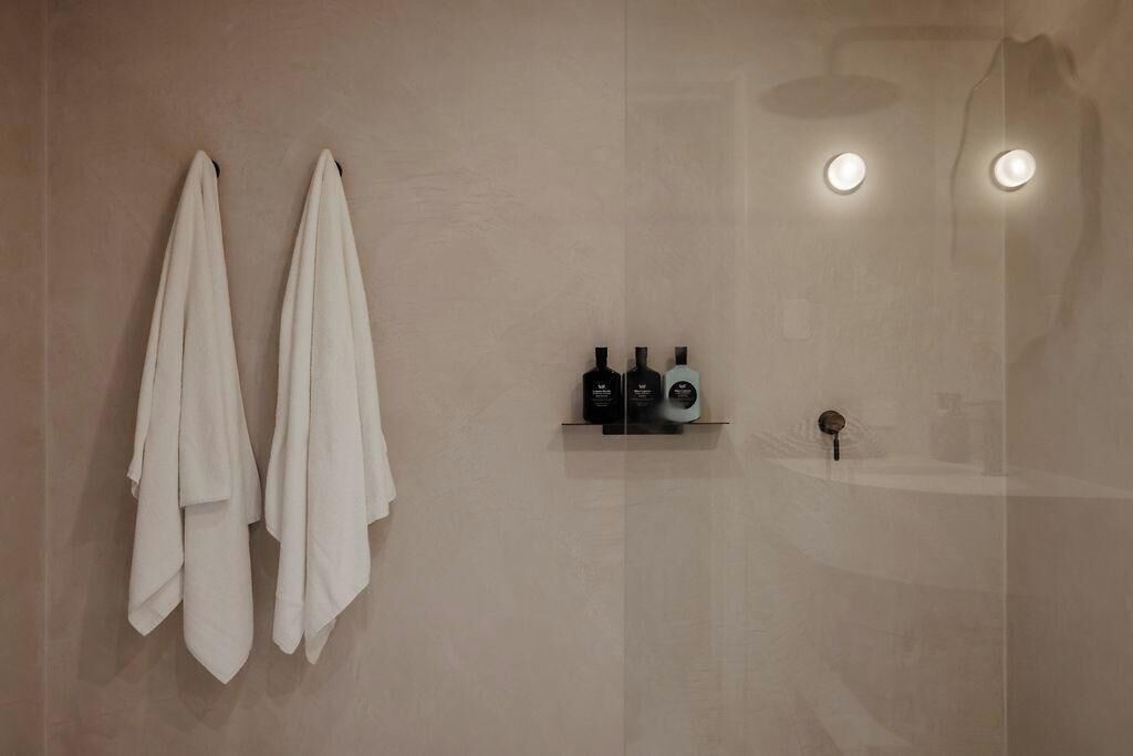 Een badkamer met twee handdoeken aan de muur, een plank met toiletartikelen en een spiegel met verlichting.