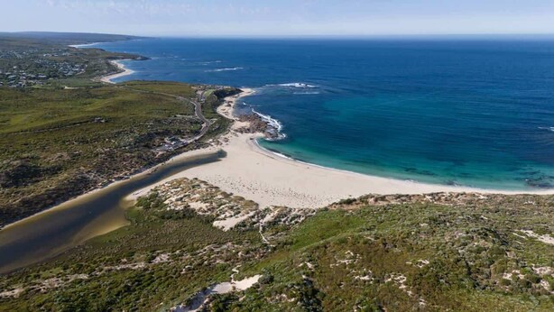 Vue aérienne d’une zone côtière avec une plage, une route et la végétation environnante.