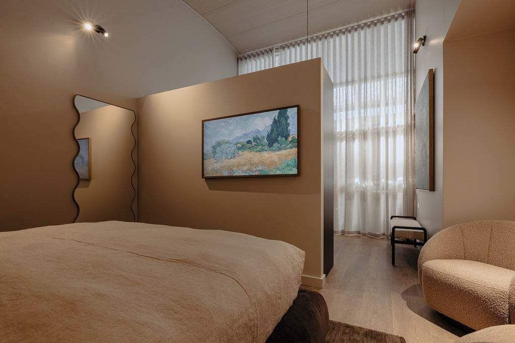 A bedroom with a large bed, a chair, a painting, and a mirror.