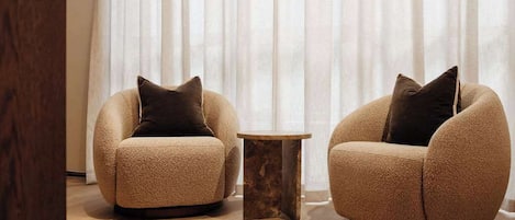 Two armchairs with dark cushions, a small wooden side table, and a large window with sheer curtains.