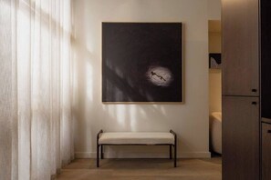 Ein Zimmer mit einer Sitzbank, einem großen abstrakten Gemälde und einem Holzkabinett.