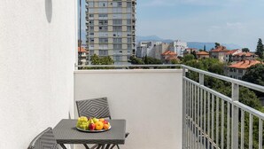 Ein Balkon mit Tisch und Stuhl, einer Obstplatte und Blick auf Gebäude und Berge.