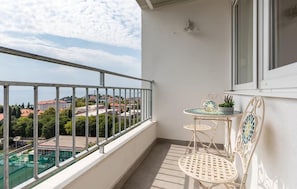 A balcony with a metal railing, a small table with chairs, a potted plant, and a view of buildings and greenery. - Amazing apartment in Split with house sea view (Split)