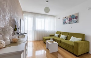 A living room with a green sofa, a white coffee table, a painting on the wall, and a window with sheer curtains. - Amazing apartment in Split with house sea view (Split)