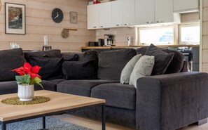 Ett modernt vardagsrum med en mörkgrå soffa, ett träbord och en vit vas med röda blommor.