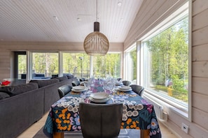A dining area with a table set for six, large windows, and a view of trees. - Villa Hellitä | Peaceful 3BR Villa with Hot Tub (Ylläsjärvi)